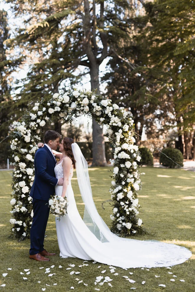 Bride and groom standing under a romantic floral arch during their wedding ceremony in Tuscany.