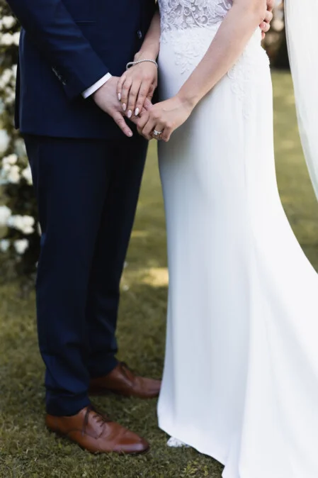 Close-up of bride and groom holding hands during their wedding in Tuscany, showing the wedding rings and elegant details of the dress, captured by photographer Vanni Frassoni