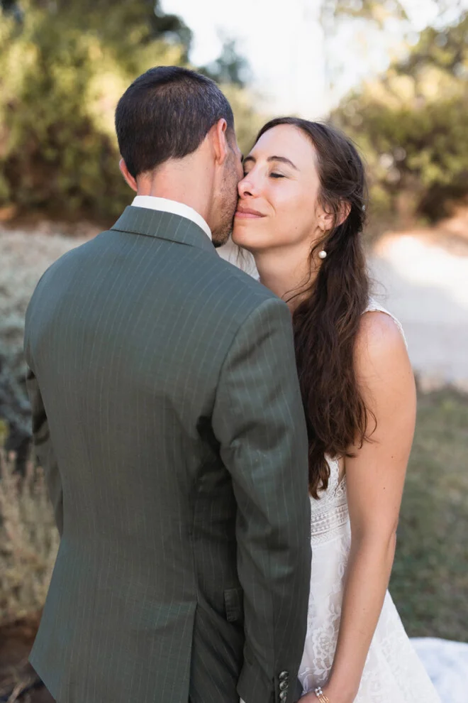 Bride smiling tenderly while the groom kisses her during their wedding at Castello di Magona in Tuscany.