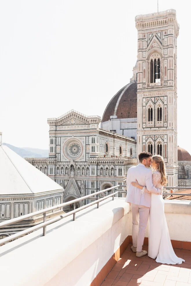 Bride and groom embracing on a terrace with a stunning view of Florence Cathedral and Giotto’s bell tower.